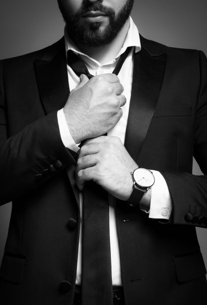 Bearded man tightening tie on grey background, closeup. Black and white effect